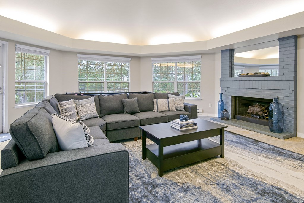 A grey couch with pillows sits in a living room with a fireplace.