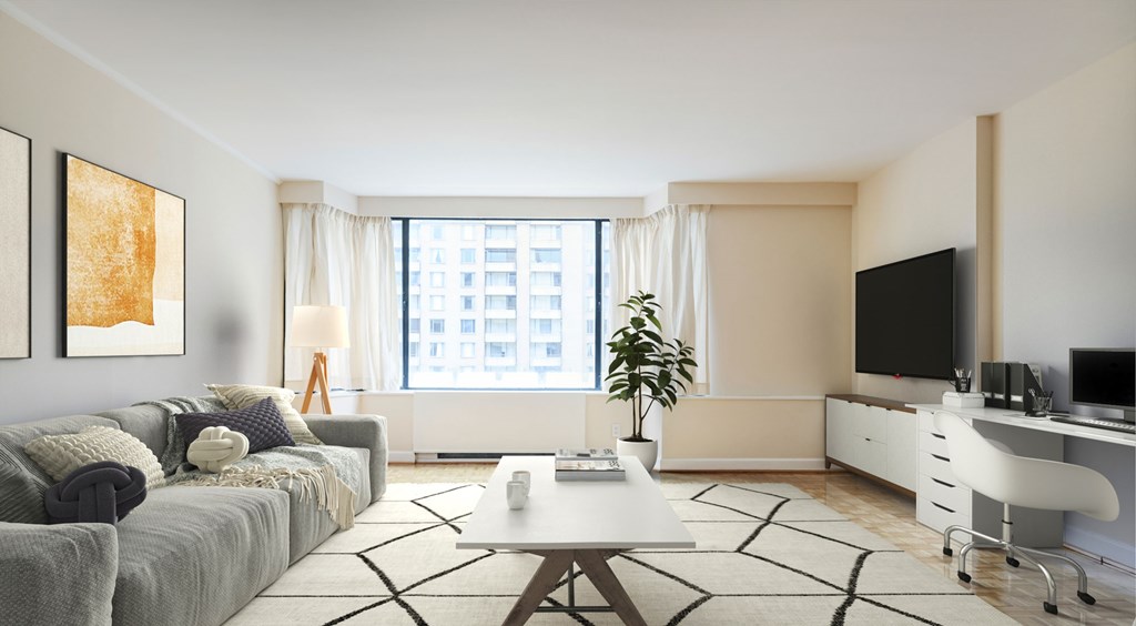 A modern living room with a grey sofa, a coffee table, a television, and a desk with a computer.