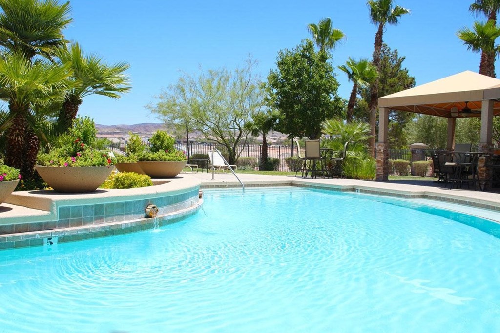 a large swimming pool with a patio with chairs and a umbrella