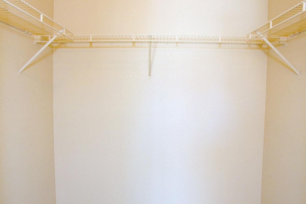 an empty closet with a white wall and a wire rack on the ceiling
