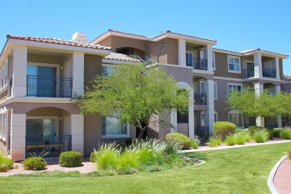 an apartment building with a lawn and trees in front of it
