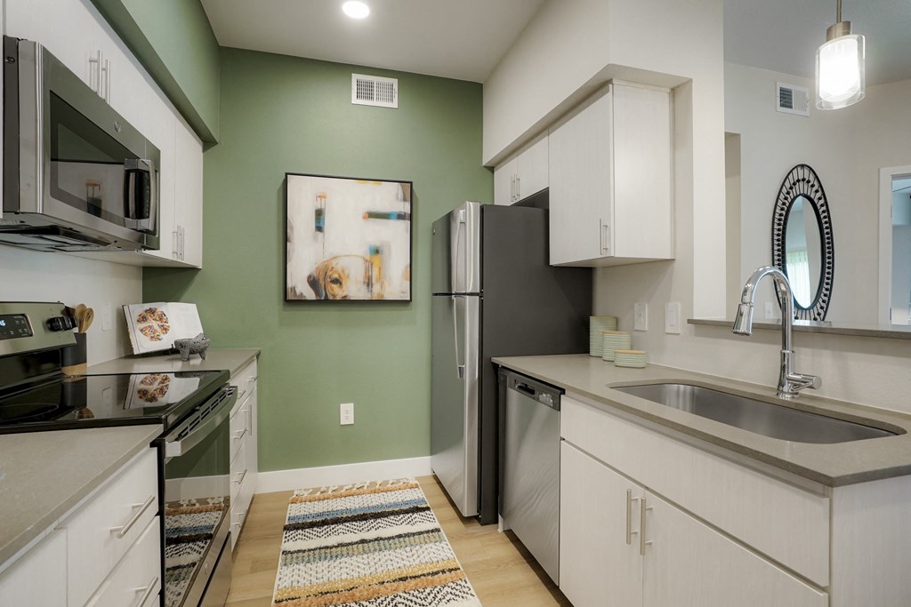 Glendale, AZ Luxury Apartments for Rent - Nacona - Kitchen With Light Countertops, White Cabinets, Wood-Style Flooring, Area Rug, Green Accent Wall, And Appliances.