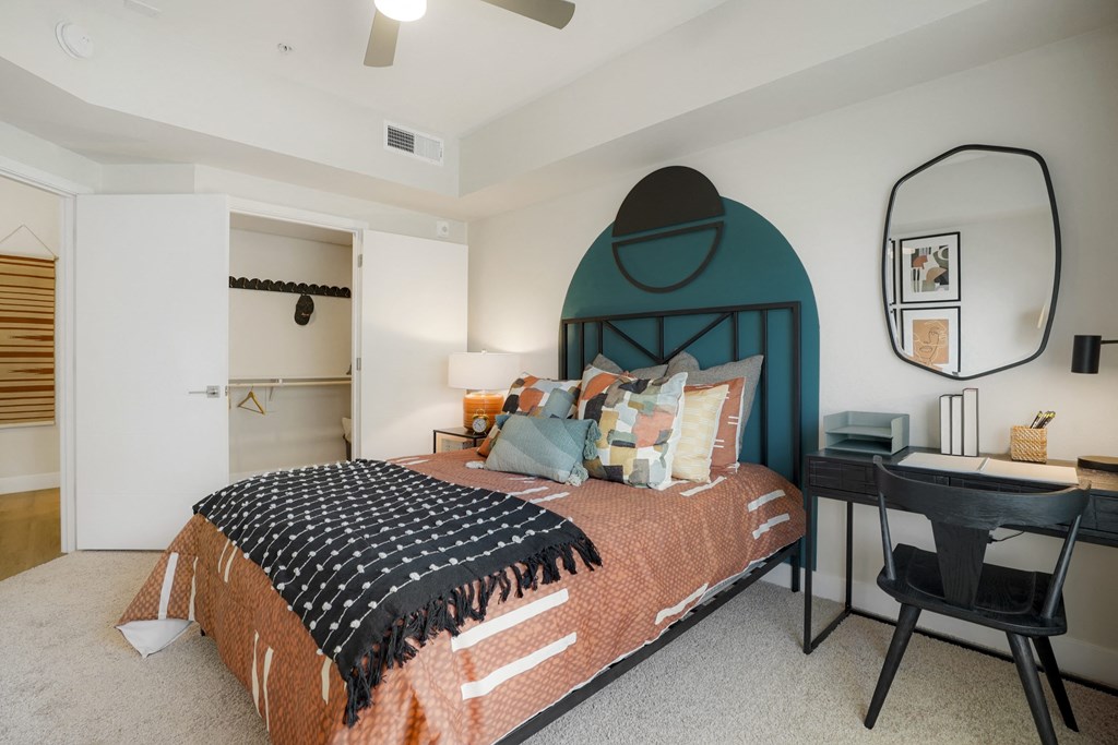 Luxury Apartments In Glendale, AZ For Rent - Nacona - Spacious Bedroom With Bed, Closet, Ceiling Fan, And Desk With Chair And Mirror.