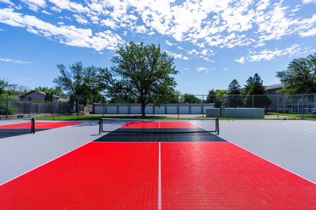 a tennis court with red and black turf and a tree