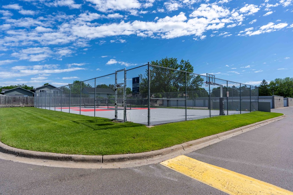 a tennis court with a chain link fence around it and a green lawn