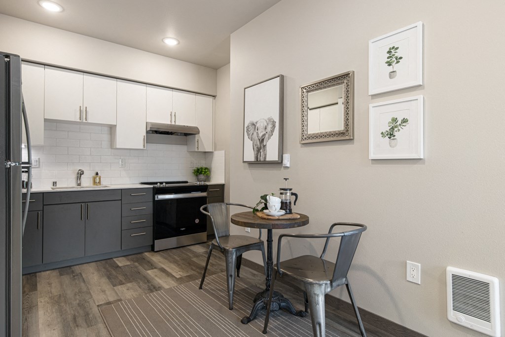 a dining area with a small table and two chairs and a kitchen in the background,