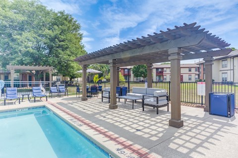 A pool area with a pergola and lounge chairs.