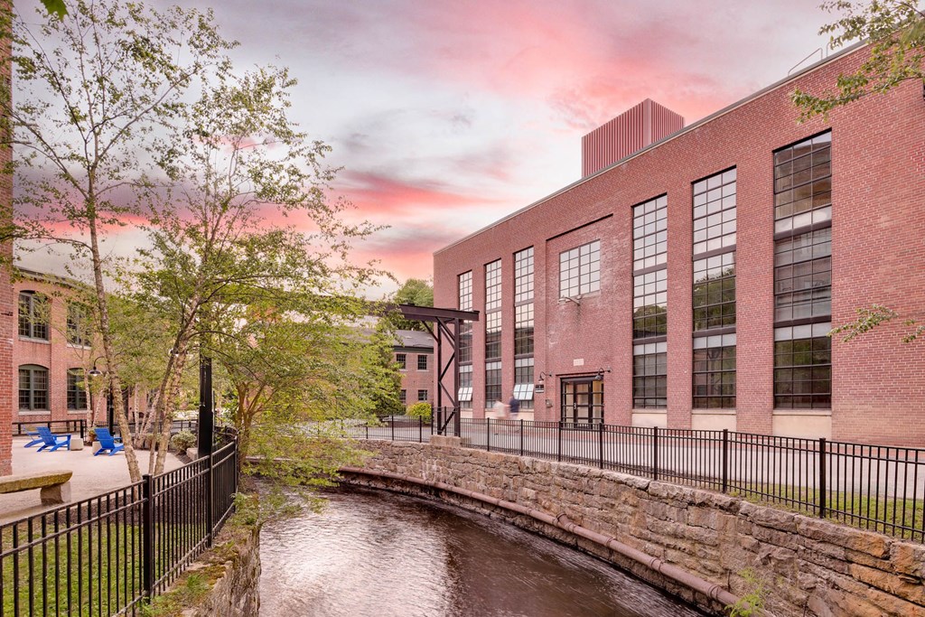 Scenic canal flowing past a red brick building with large windows at sunset.