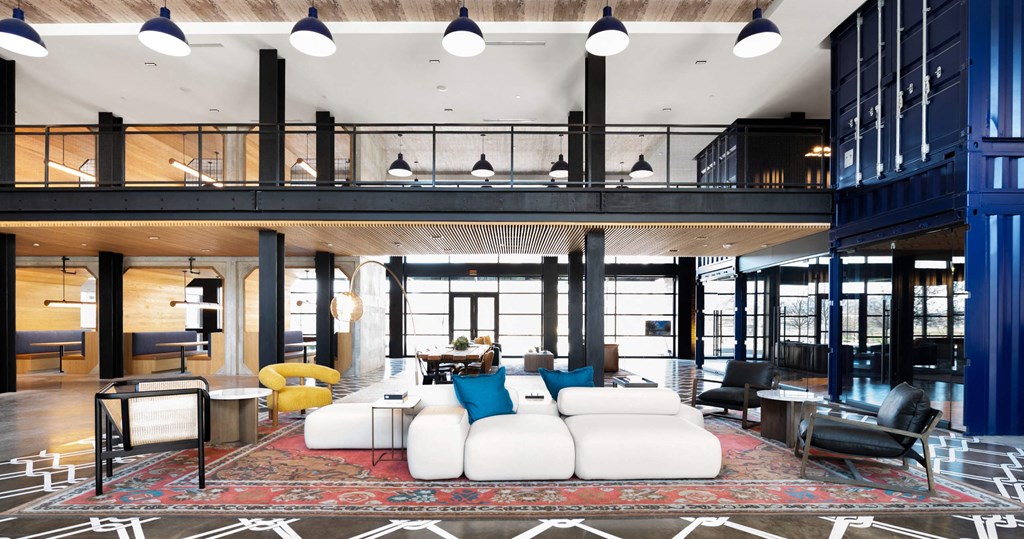 A large, open community lounge with a high ceiling and a mix of modern and industrial design elements.