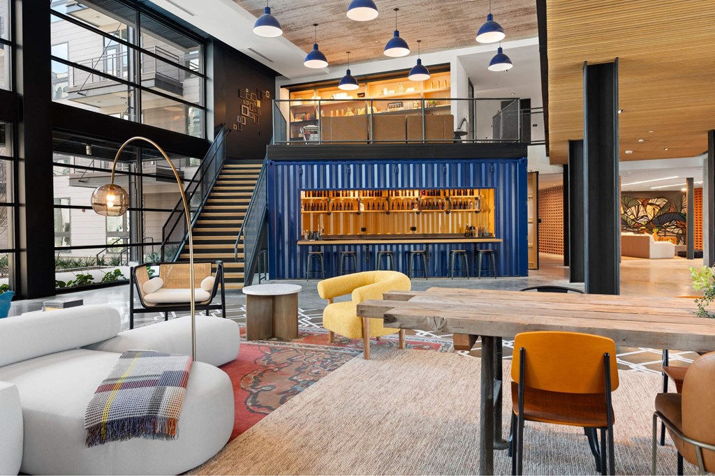 A modern interior with a staircase, chairs, and a table inside The Laura community lounge.