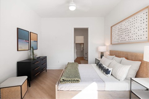 Downtown Houston, TX, Apartments with In-Unit Washer and Dryer - The Laura - Bedroom With A Woven Headboard Bed, White Bedding And Green Throw, Matching Nightstand Lamps, and Black Dresser.