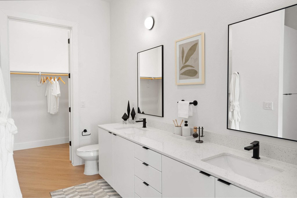 A white bathroom with a toilet, sink, and mirror at The Laura apartment complex in Houston, TX.