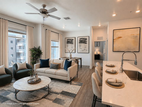 A modern living room with a white sofa set, a coffee table, and a kitchen area with a sink and countertop.