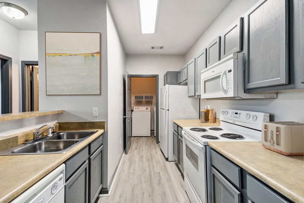 Nashville, TN Apartments - Parc at Metro Center - long kitchen with white appliances and wooden floors and Grey Cabinets