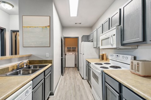 a long kitchen with white appliances and wooden floors and white cabinets