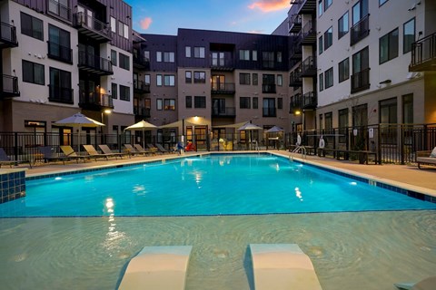 Dog-Friendly Apartments in Wheat Ridge, CO - The Parallel - Swimming Pool With Lounge Chairs, Umbrellas, Fenced Deck, Balconies, And Surrounding Apartment Buildings.