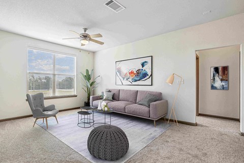A living room with a grey sofa, a grey chair, a grey ottoman, a small table, a potted plant, a painting, a floor lamp, and a window with blinds.