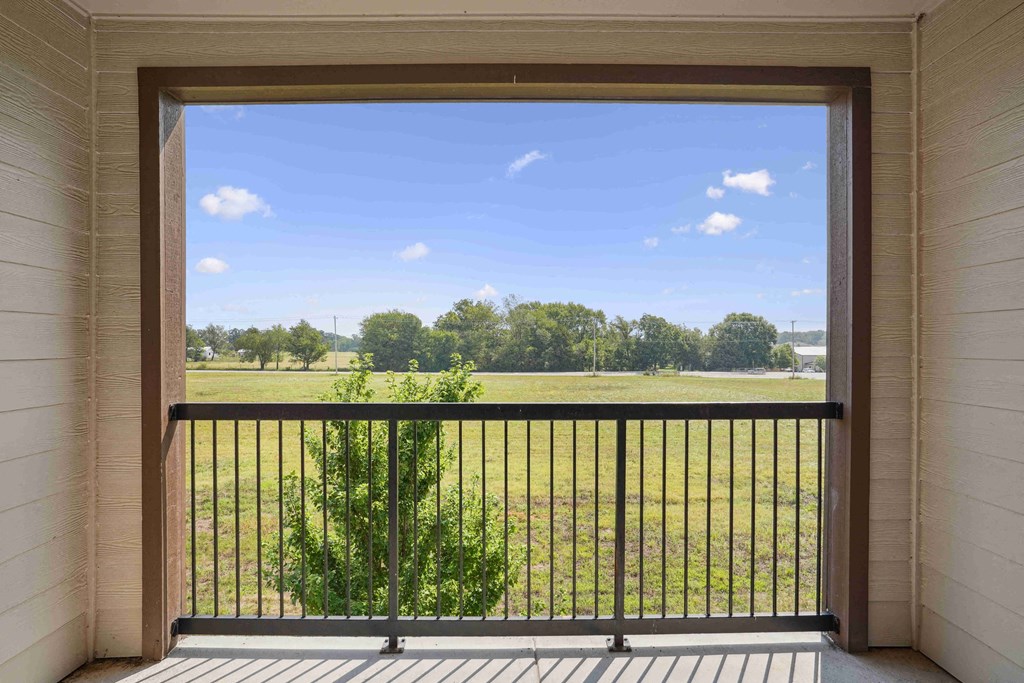 A balcony with a black railing and a view of a green field.
