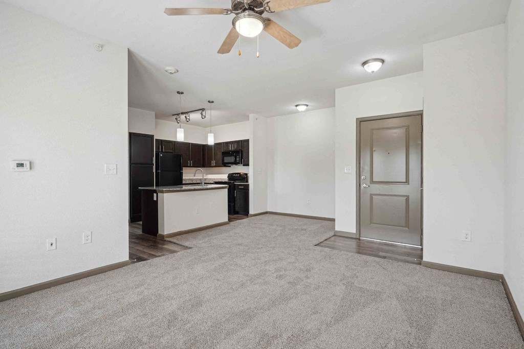 Apartments for Rent in Bentonville, AR 72713– Parc at Bentonville -   A spacious living room with a ceiling fan and a kitchen in the background.