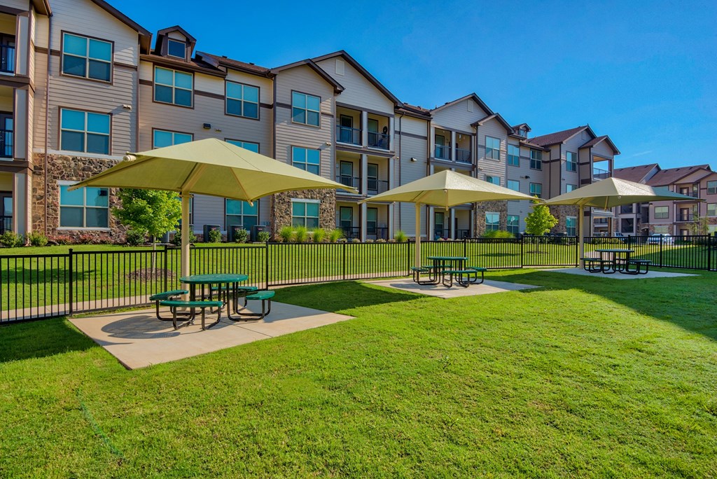 Park with tables and umbrellas and grass and building in back