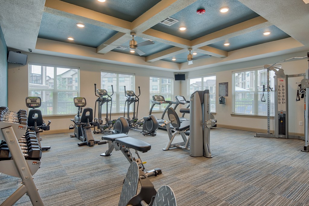 Apartments for Rent in Bentonville, AR 72713– Parc at Bentonville -   Gym with lifting equipment and cardio equipment with ceiling lights and glass windows
