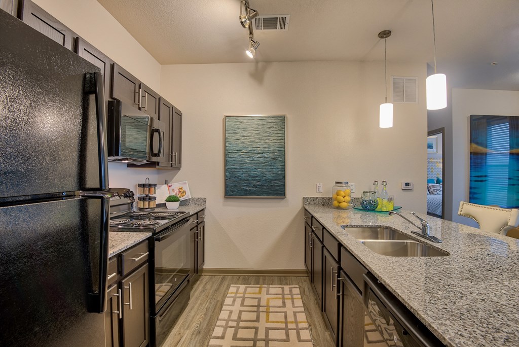 Kitchen area with sink and fridge and stove top and chairs and hanging lights and marble kitchen top