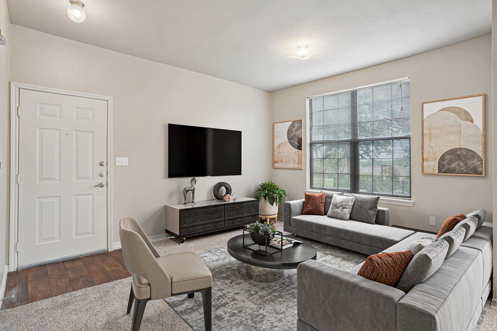 1, 2 & 3-Bedroom Apartments for Rent in Maumelle, AR – Parc at Maumelle – A living room with a grey couch, a white door, a black TV and a plant on the coffee table.