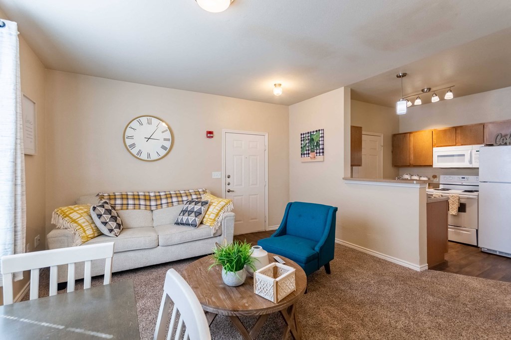 Living room with a ceiling light and carpet floor and window with blinds and kitchen in background with wood floor