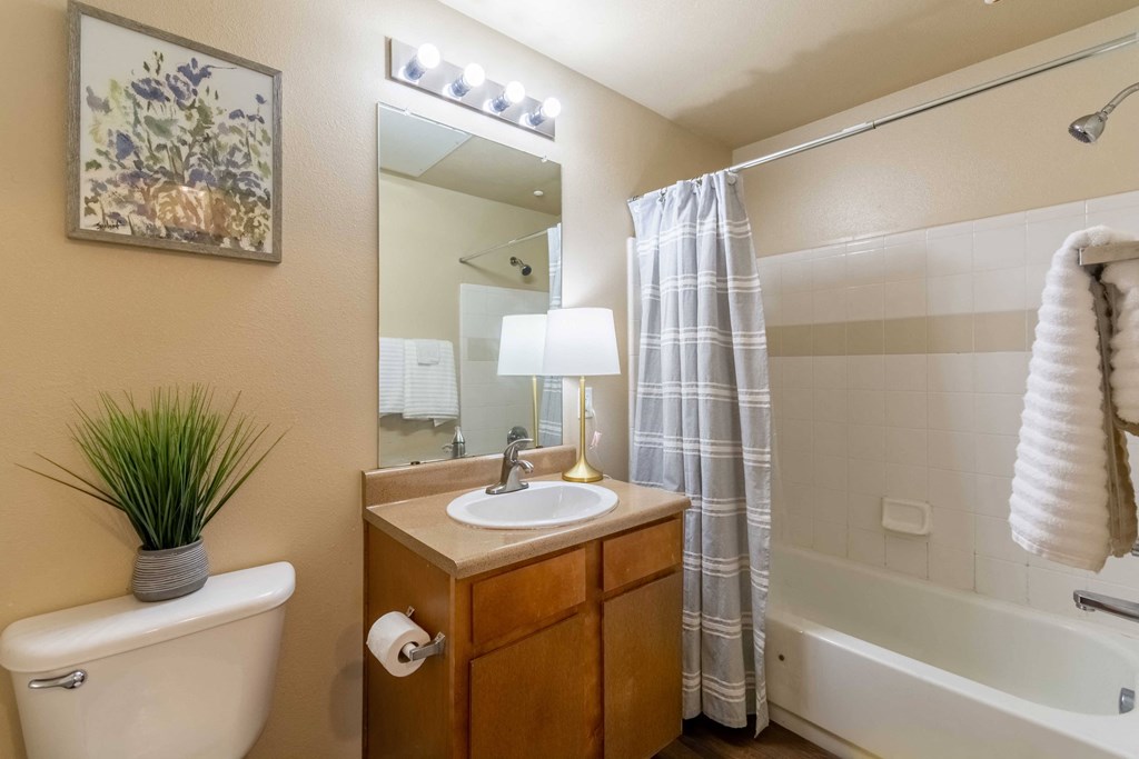 A bathroom with a toilet and sink with wood cabinets and wood floor and bathtub