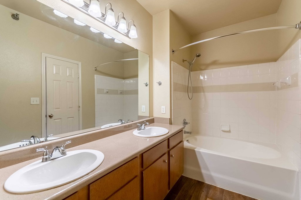 A bathroom with double vanity and big mirror and ceiling lights and bathtub