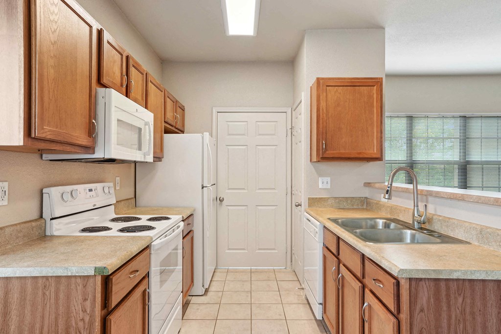 1, 2 & 3-Bedroom Apartments for Rent in Rogers, AR – Parc at Rogers– A kitchen with white appliances and wooden cabinets.