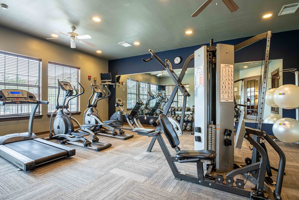 Apartments for Rent in Rogers, AR 72758– Parc at Rogers-   gym with lifting and cardio equipment with a big mirror and windows