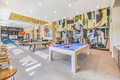 a game room with a pool table and tables in front of a colorful wall