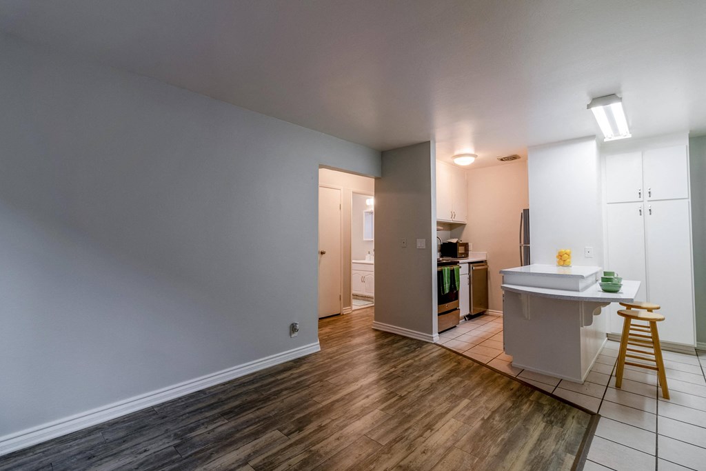 an empty living room and kitchen with wood flooring and a white counter with a