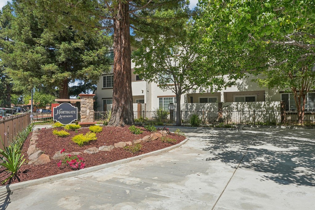 a sidewalk in front of a building with trees and a sign