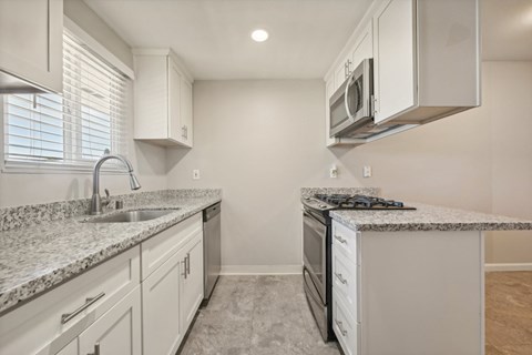 a kitchen with white cabinets and granite counter tops and a stove and microwave