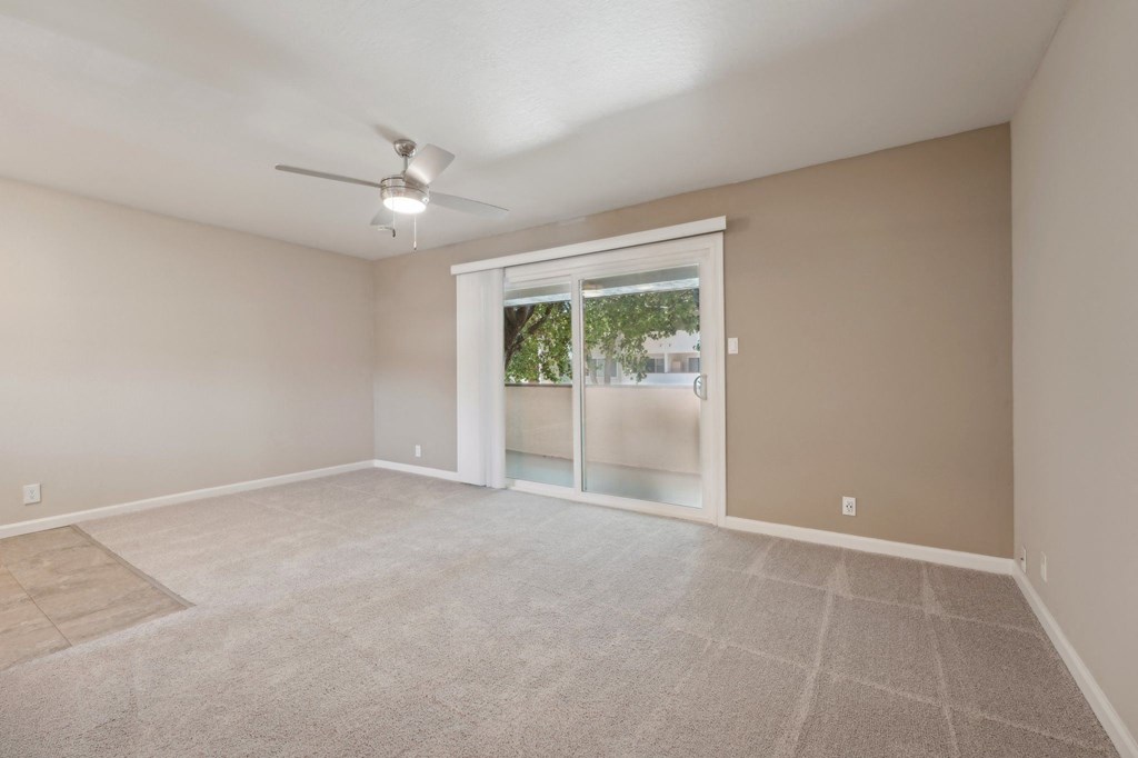 an empty living room with a large window and a ceiling fan