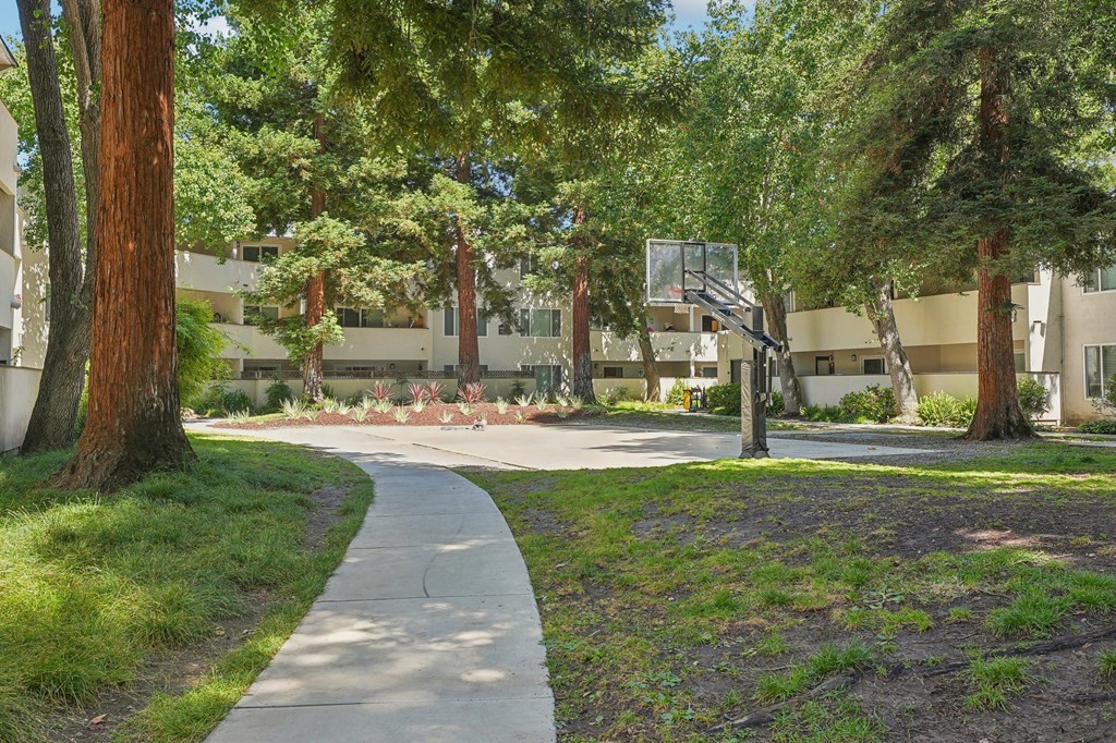 a sidewalk in front of an apartment building with a basketball court