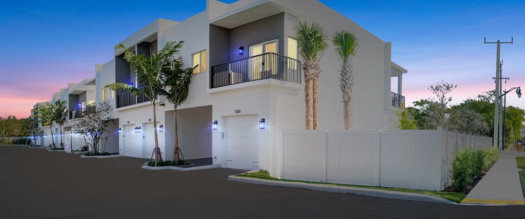 Modern white townhouses with balconies and palm trees at dusk.