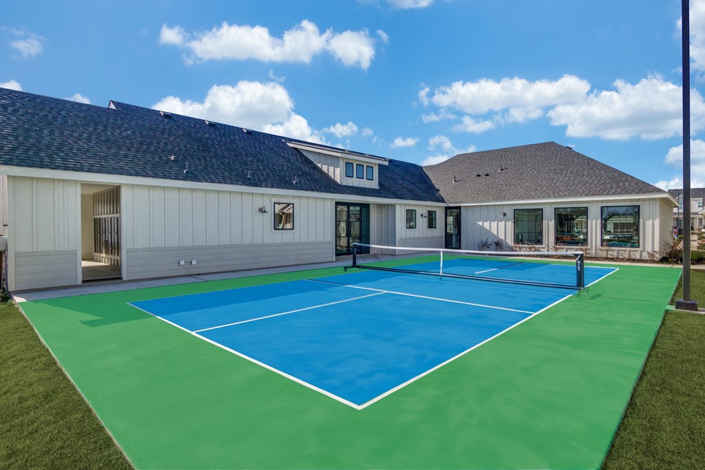 A tennis court is surrounded by a white building and a green lawn.
