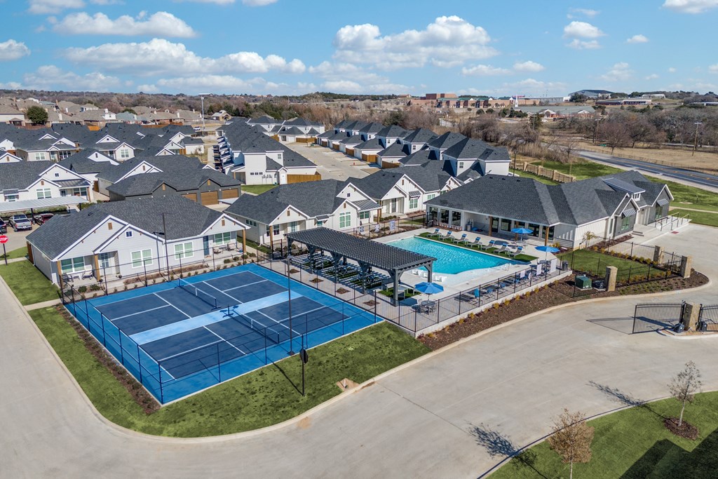 A tennis court is surrounded by houses in a residential area.