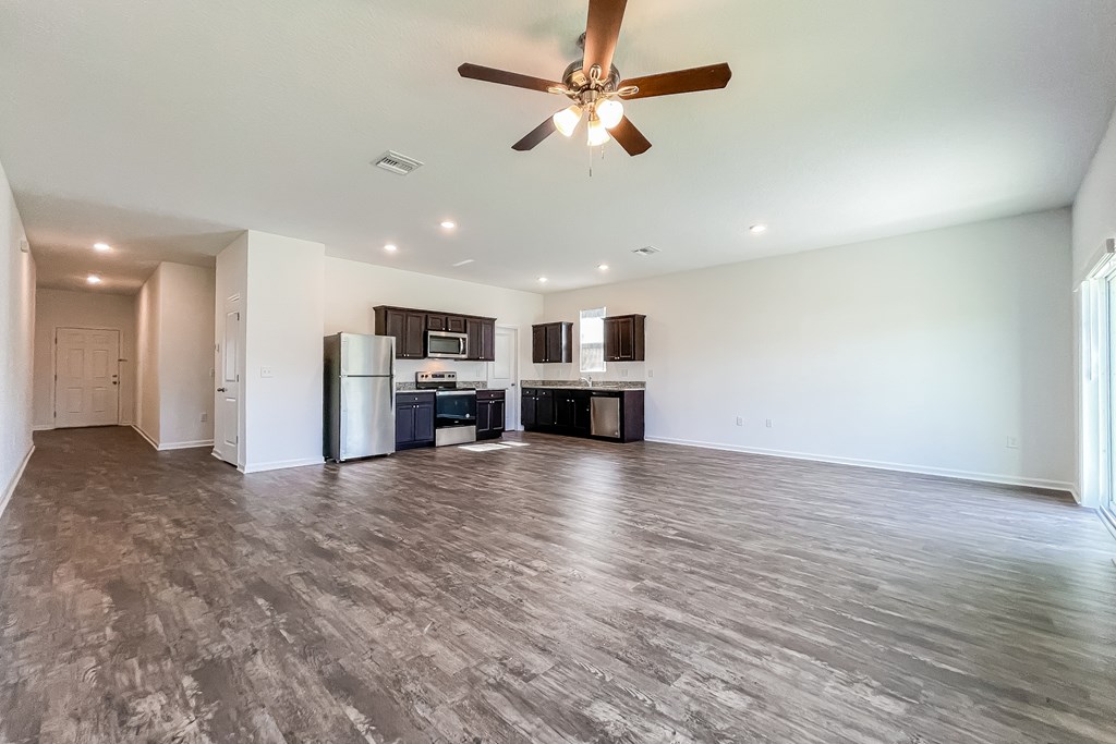 A spacious room with a ceiling fan and a kitchen area with appliances.