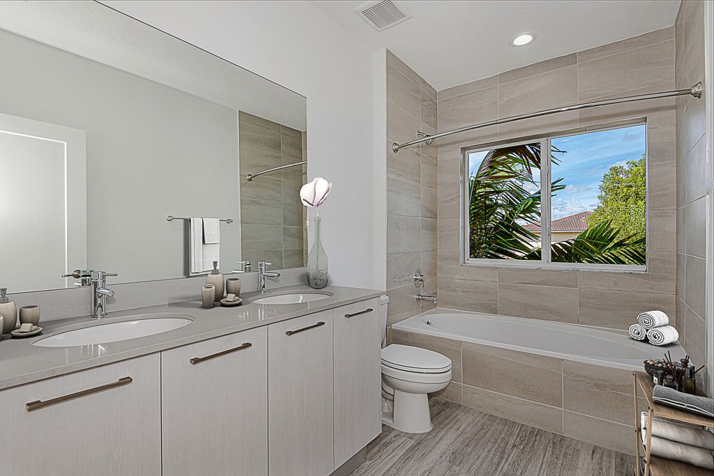 Modern bathroom with double vanity, bathtub, and window overlooking palm trees.