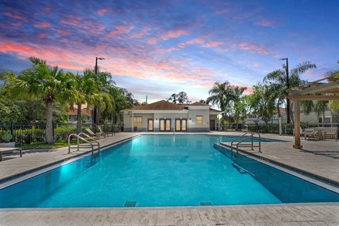 A large swimming pool surrounded by palm trees and a building in the background.