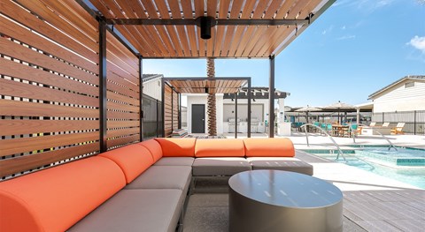 A wooden pergola with orange cushioned seating.