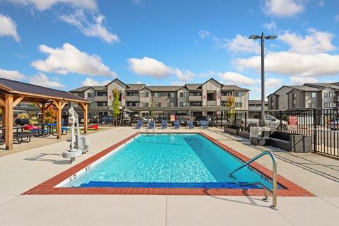 Dog-Friendly Apartments in Vancouver, WA - Prairie Home Apartments - Resort-Style Swimming Pool With Lounge Seating, Couch, Covered Pavilion, Fenced Deck, and Apartment Buildings.