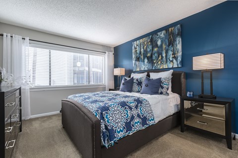 A bedroom with a bed, nightstand, and a window with blinds.