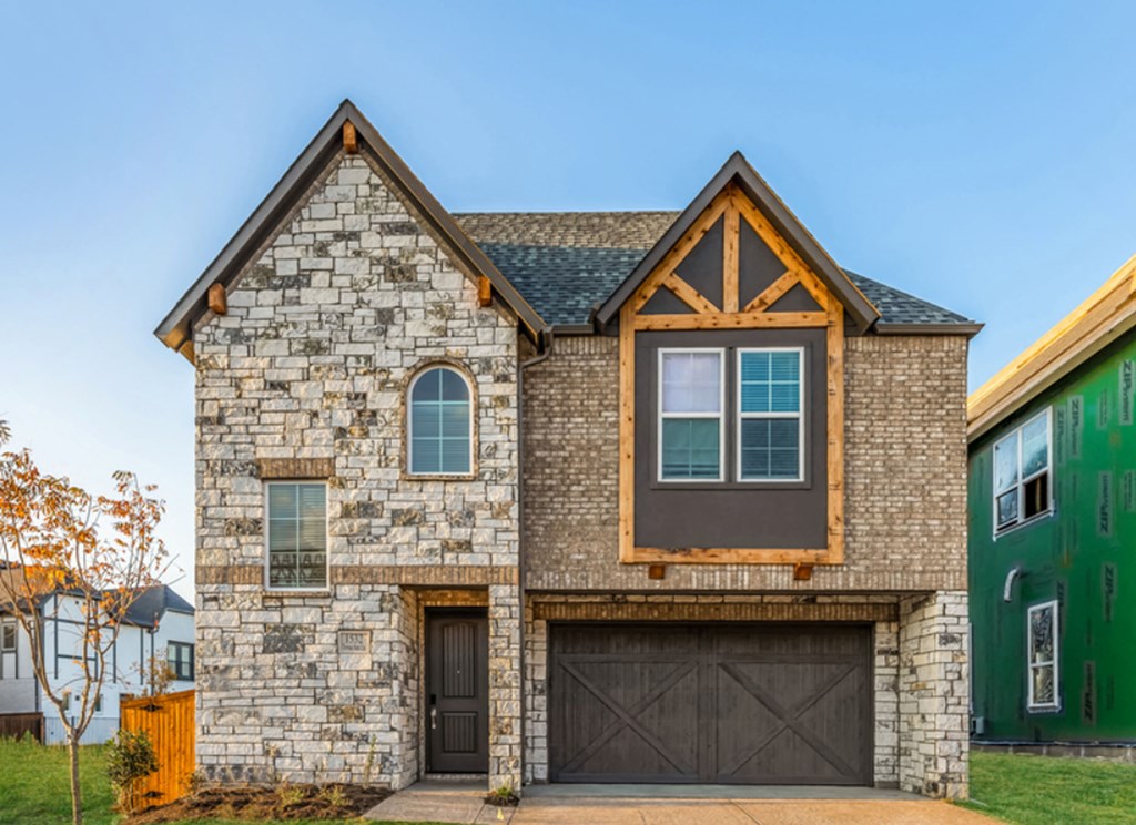 Allen, TX, Rental Homes Near Craig Ranch - Ridgeview Villas - The Exterior of A House, Featuring Gray Stone Walls, Modest Windows, Brown Front Door, and Wooden Two-Door Garage Surrounded By Beautiful Landscaping