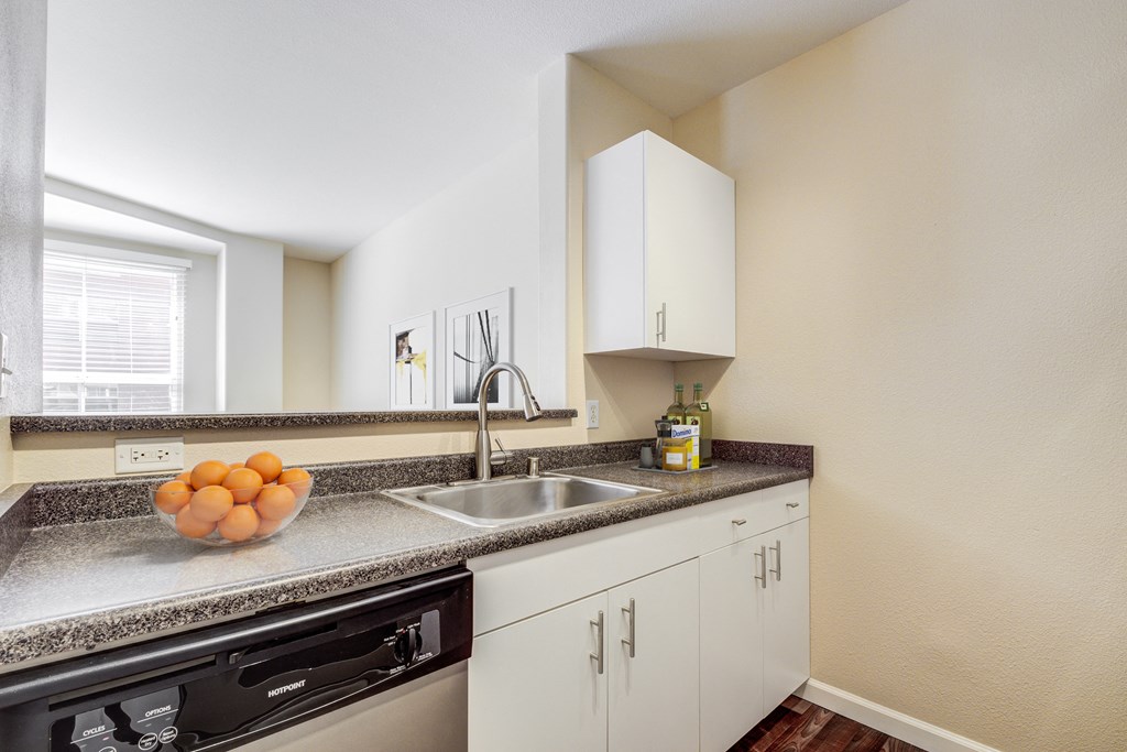 a kitchen with white cabinets and a sink and a bowl of fruit