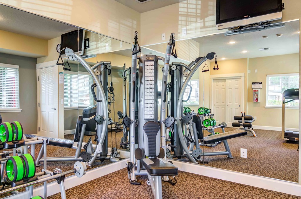 Apartments For Rent in Vancouver, WA - Reflections at the Park - 24-Hour Fitness Center With Workout Equipment, Mirror Walls, And TV Screen.